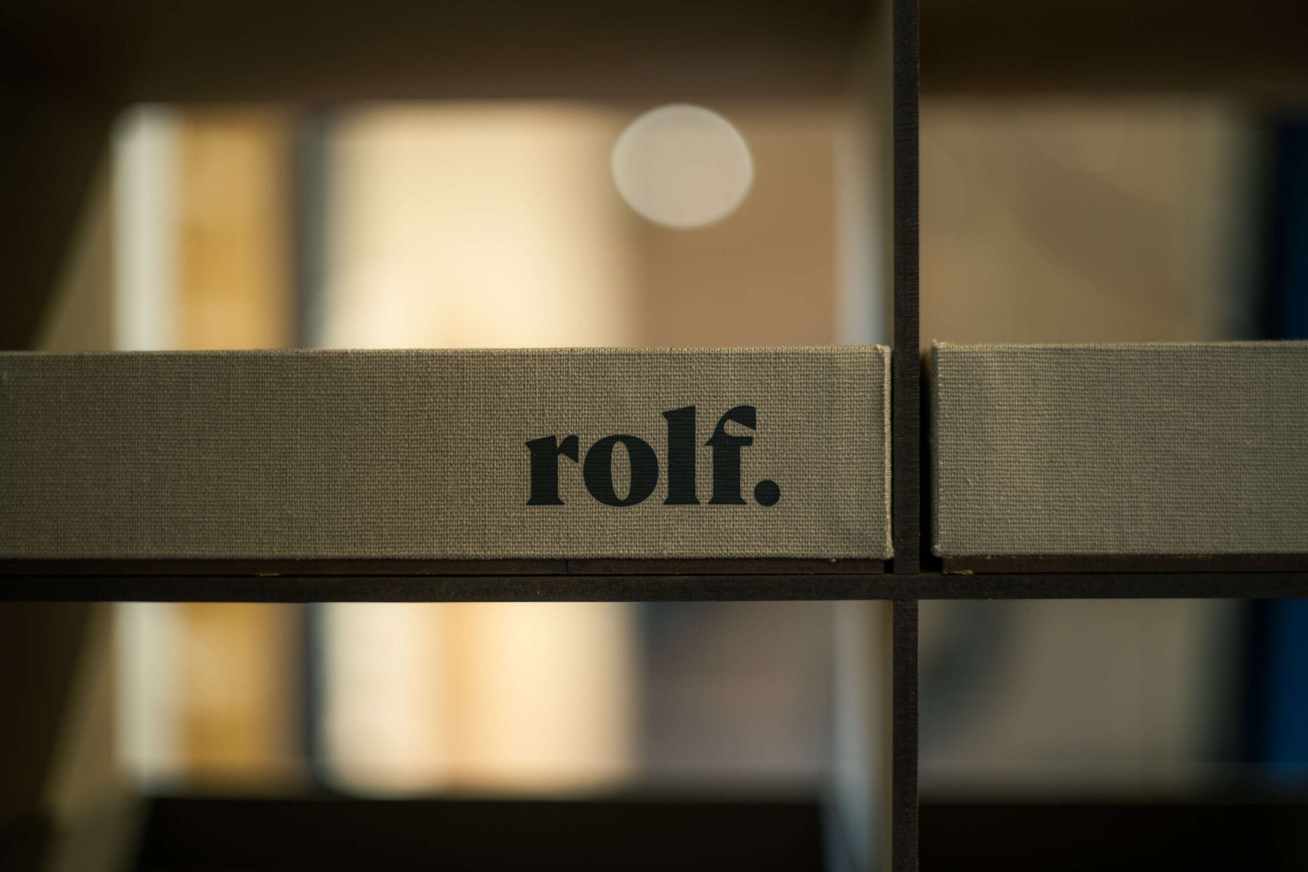 Detailaufnahme eines Leinenbandes mit "rolf." Schriftzug, scharf im Vordergrund mit weichem, beigeleuchtetem Hintergrund, der ein Gefühl von modernem Design und Schlichtheit ausstrahlt.