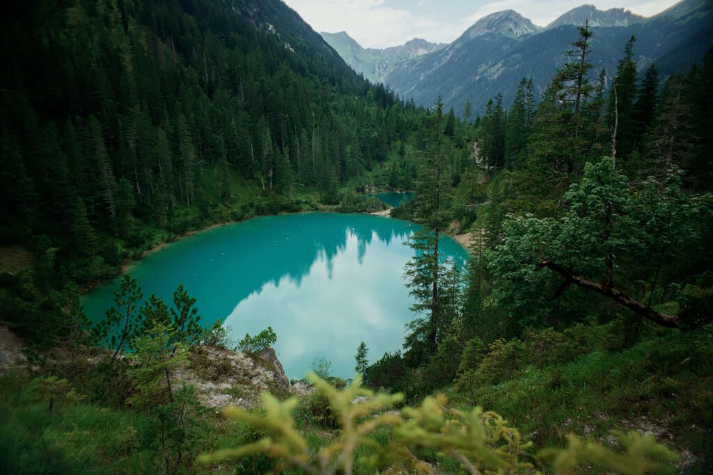 Ein idyllischer Bergsee mit kristallklarem, grünem Wasser, eingerahmt von üppigen Wäldern, die zum Schutz und zur Schonung der Augen beitragen.