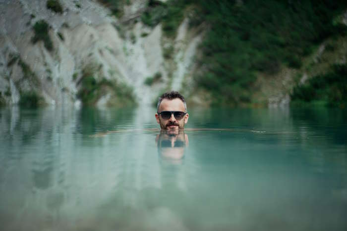 Mann mit Bart und Sonnenbrille schwimmt im klaren Bergsee