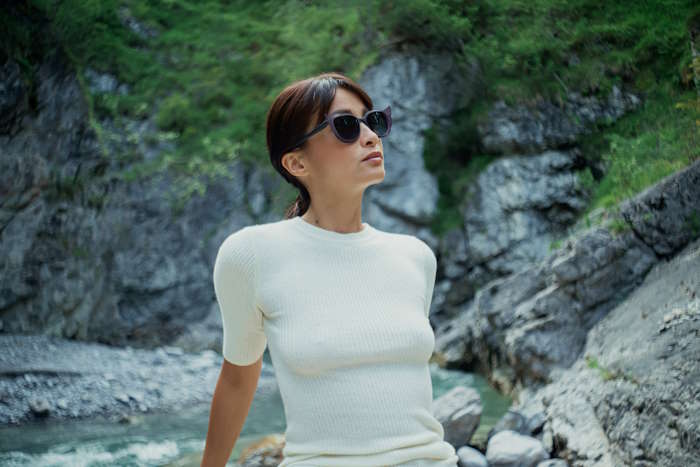 Elegante Frau mit Sonnenbrille mit Tönung vor einer felsigen Flusslandschaft