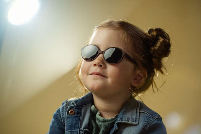 Kleinkind mit lächelndem Gesichtsausdruck trägt Sonnenbrille mit Tönung
