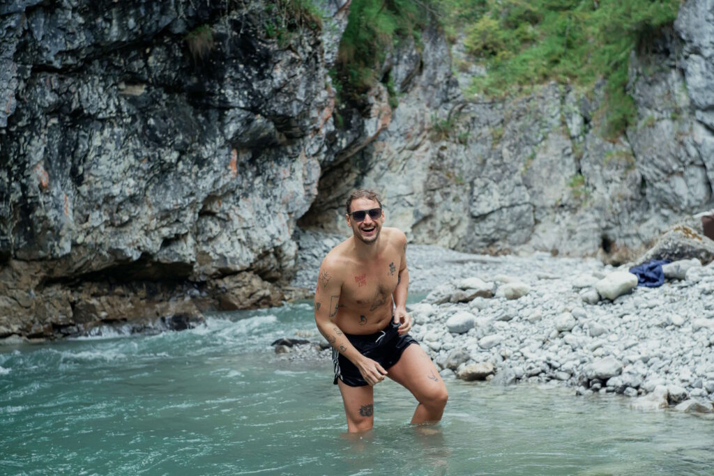 Fröhlicher Mann wadet in einem Gebirgsfluss mit einer Sonnenbrille mit Tönung