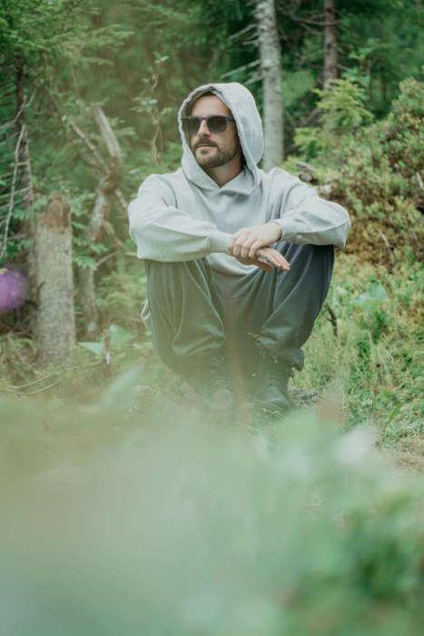Mann mit Sonnenbrille sitzt im Wald, Schutz vor Bindehautentzündung durch UV-Strahlung