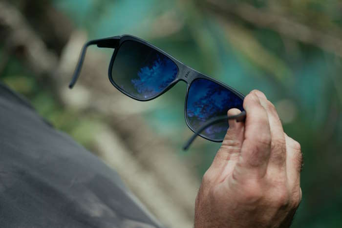 Hand hält Sonnenbrille mit blauer Tönung im Outdoor-Setting – Tönung bei Sonnenbrillen