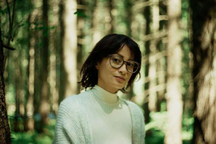 Nachdenkliche Frau mit einer Holzbrille von Rolf steht im dichten Wald