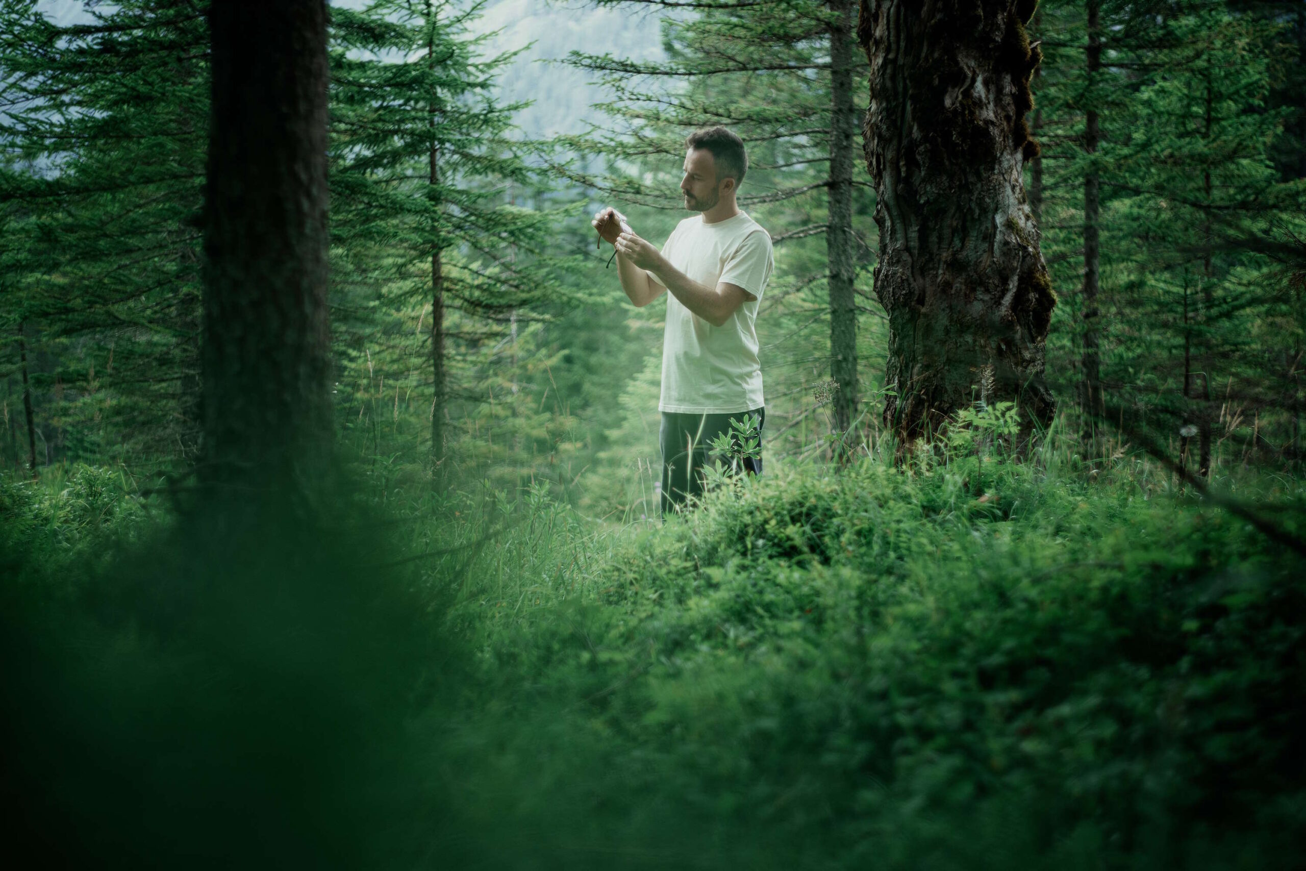 Mann in weißem Shirt betrachtet seine wiedergefundene Brille in seinen Händen im dichten Wald