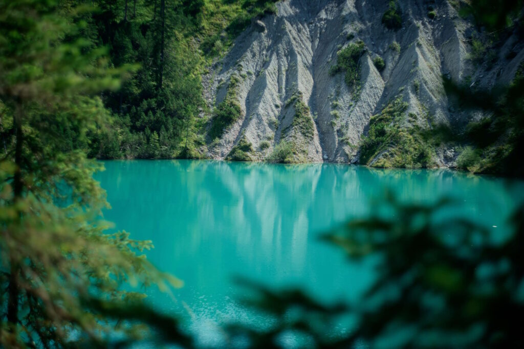 Ein smaragdgrüner Bergsee umgeben von steilen Felswänden und dichten Wäldern, gelbe Augen durch Alkohol.
