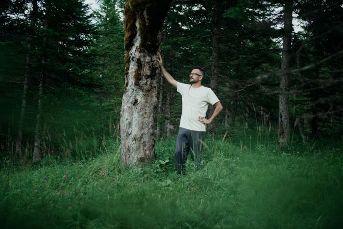 Ein Mann lehnt an einem Baum in einem dichten Wald