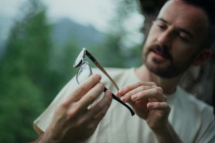 Ein Mann hält eine Brille in der Hand und untersucht sie im Wald.