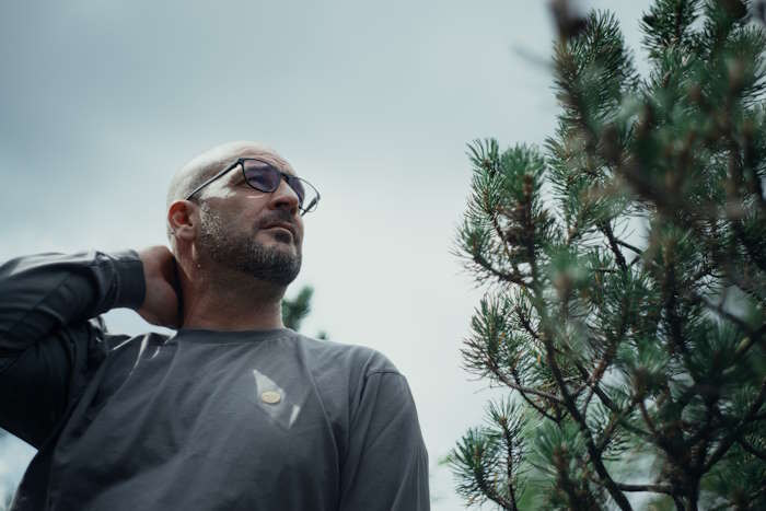 Ein Mann mit Glatze und Brille steht im Freien, umgeben von Bäumen. - zum Thema "verschwommen sehen"
