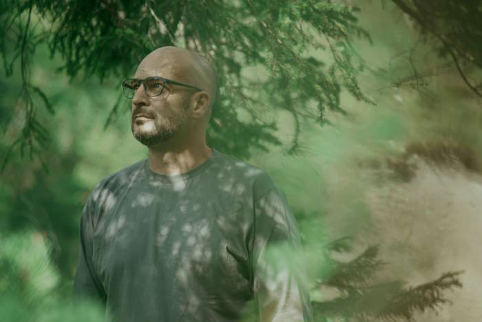 Ein Mann mit Brille steht in einem dichten Wald und blickt nachdenklich, gelbe Augen durch Alkohol.