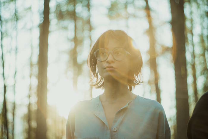 Frau mit Brille im Wald bei Sonnenuntergang, die Iris ihrer Augen ist erkennbar.