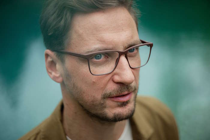 Ein Mann trägt eine Männerbrille für den Sommer und blickt nachdenklich über einen türkisfarbenen See.