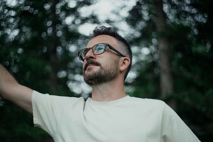 Mann mit Brille hebt den Arm im Wald – Männerbrillen für den Sommer.