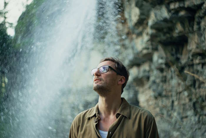 Mann mit Brille steht nachdenklich vor einem Wasserfall