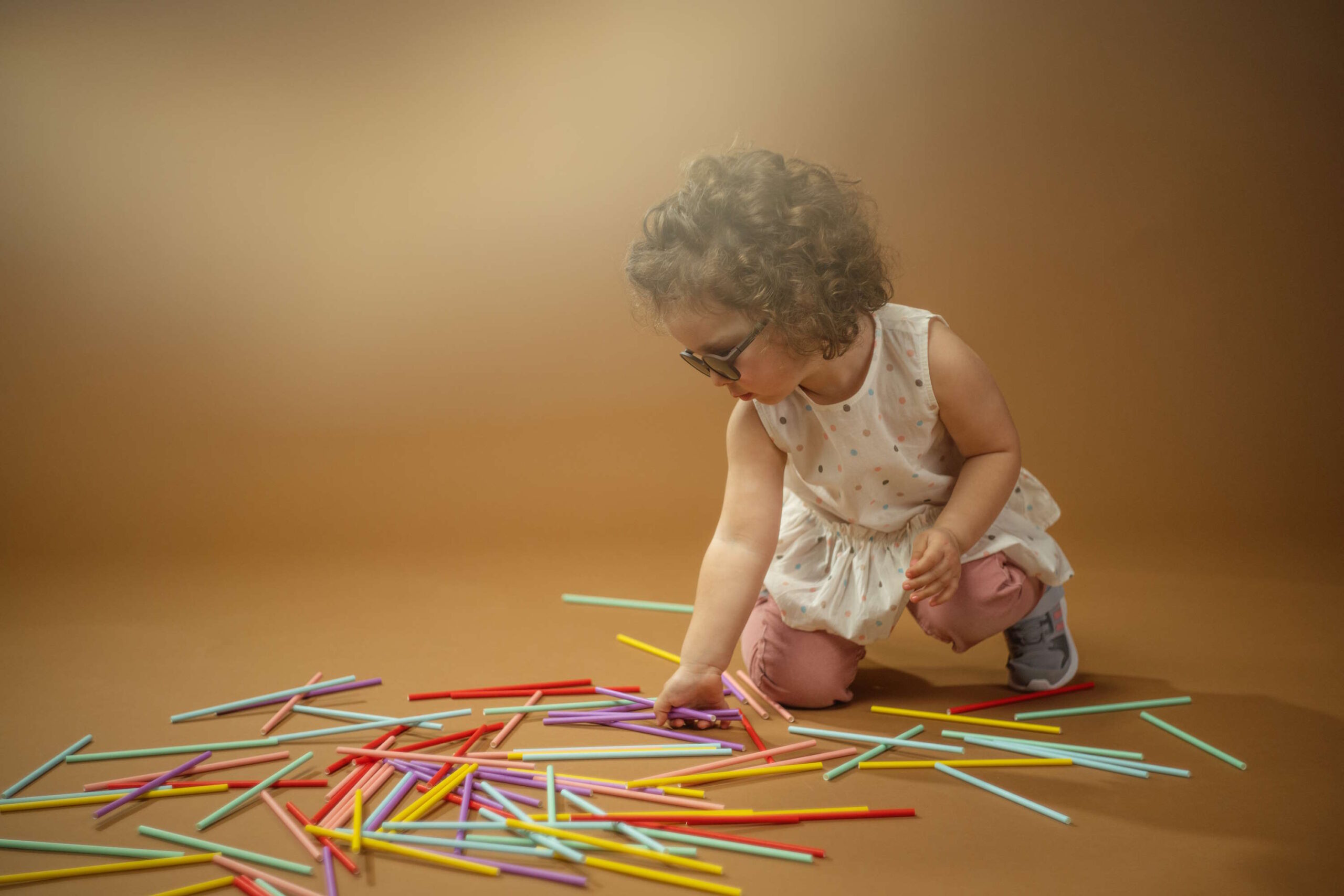 Kleines Mädchen spielt mit bunten Stäbchen und trägt Kinderbrillen für die Ferien