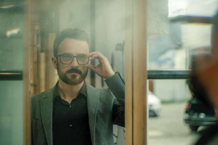 Ein Mann mit Brille betrachtet sein Spiegelbild, während er eine Augenübung für Bildschirmarbeit durchführt.