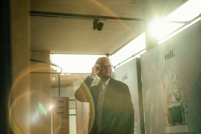 Ein Mann mit Brille steht in einem Raum mit Sonnenlicht, während er über Augenübungen für Bildschirmarbeit nachdenkt.