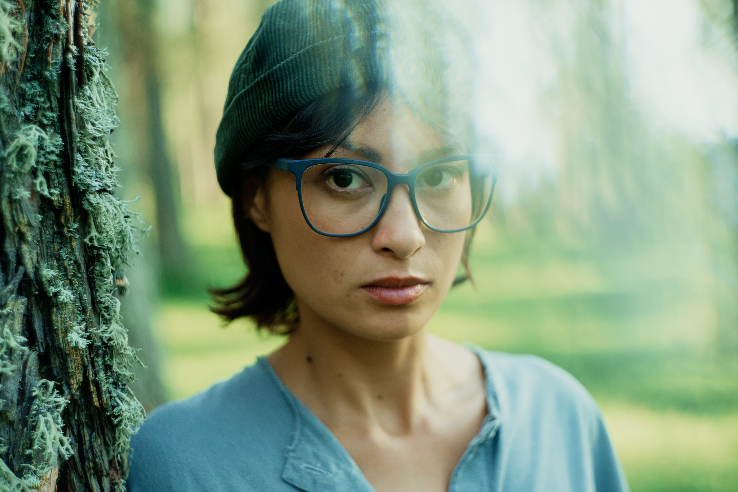 Frau mit blauer Brille und grünem Hut im Wald, ideal für Damenbrillen für den Sommer