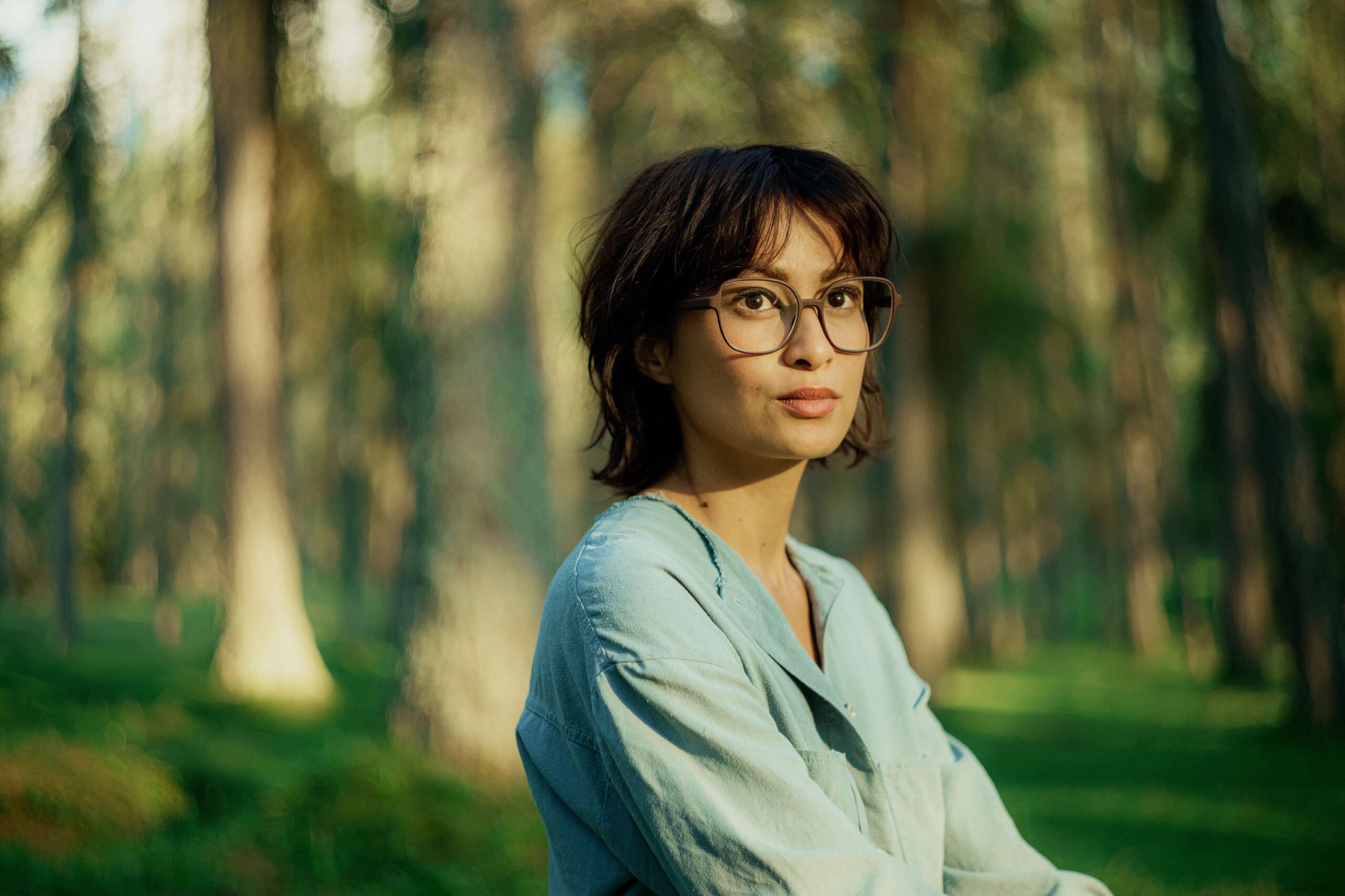 Frau in blauem Hemd und Brille im Wald, passend für Damenbrillen für den Sommer