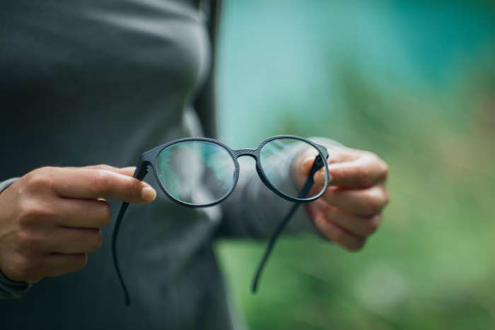 Person hält eine dunkle Brille in den Händen, überlegt welche Brillenfarbe zu welchem Typ passt.