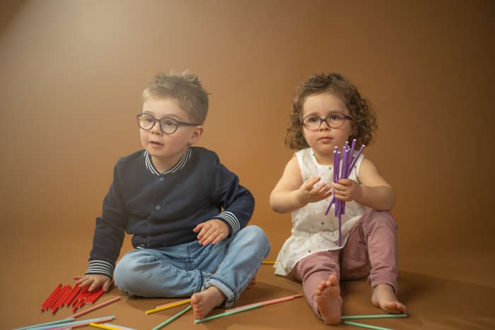 Zwei Kinder mit Brille im Kindergarten, sitzend auf dem Boden mit bunten Stiften.