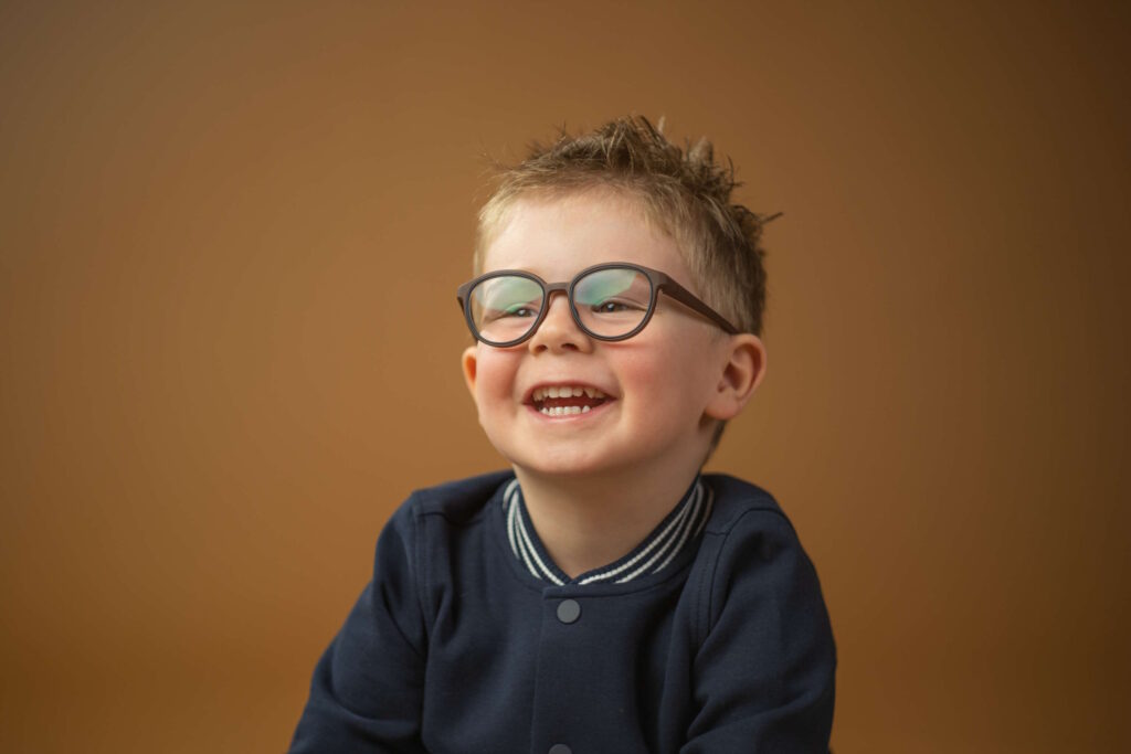 Lächelndes Mädchen mit Brille im Kindergarten, vor neutralem Hintergrund.