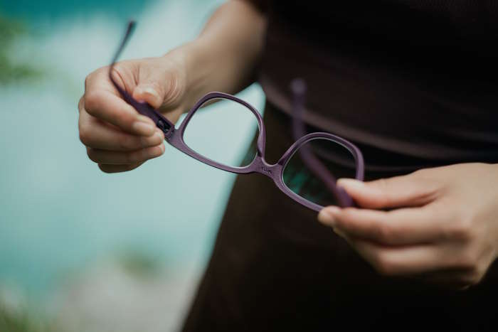 Person hält eine lilafarbene Brille in den Händen, überlegt welche Brillenfarbe zu welchem Typ passt.