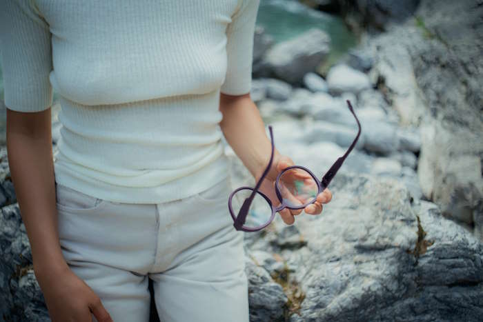 Person in heller Kleidung hält eine lilafarbene Brille in der Hand, überlegt welche Brillenfarbe zu welchem Typ passt.