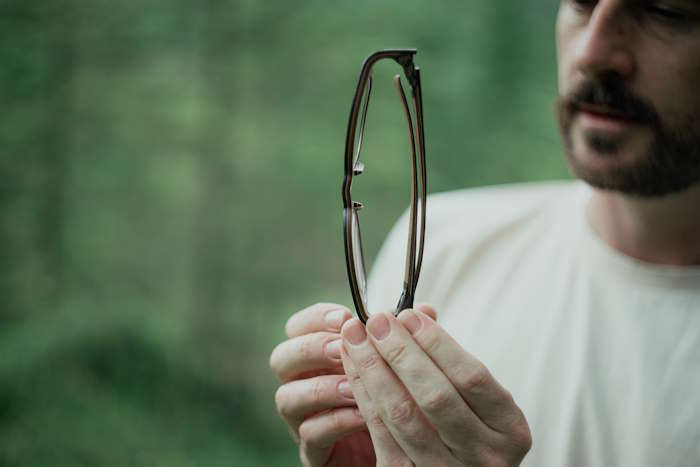 Aufbau einer Brille, Person betrachtet eine zusammengeklappte Brille, Fokus auf den Faltmechanismus und die Bügel.