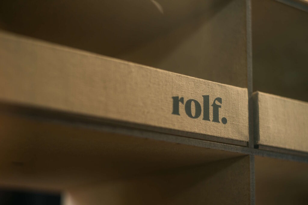 Nahaufnahme des Schriftzugs „rolf“ auf einer strukturierten Oberfläche eines Regals.