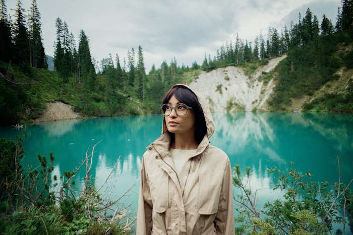 Frau mit Brille für schmale Gesichter vor einem türkisfarbenen Bergsee und bewaldetem Hintergrund