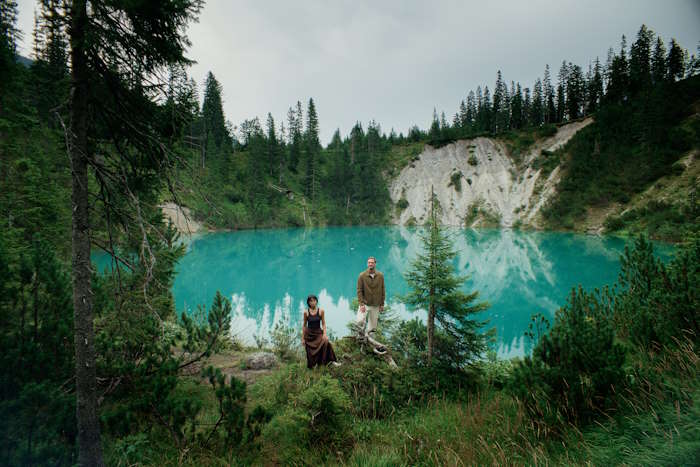 Paar steht vor einem türkisfarbenen Bergsee, umgeben von Nadelbäumen und Felsen