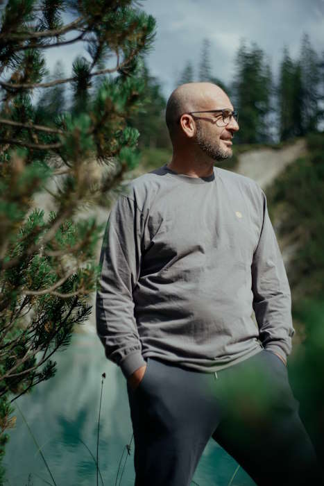 Ein Mann in entspannter Haltung vor einer malerischen Wald- und Wasserlandschaft – Fakten übers Sehen.