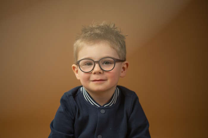 Porträt eines lächelnden Jungen mit Brille und blauer Jacke vor einem neutralen Hintergrund. Augenfarbe bei Babys