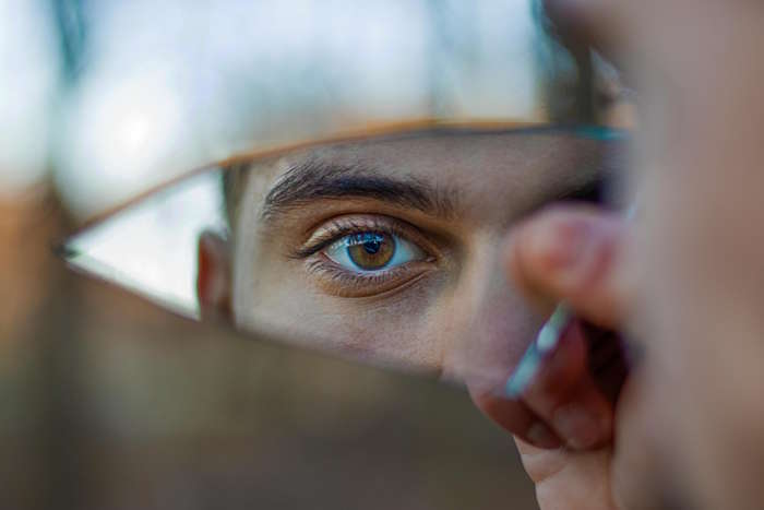 Auge eines Mannes, reflektiert in einem zerbrochenen Spiegel, mit Fokus auf Augenform.