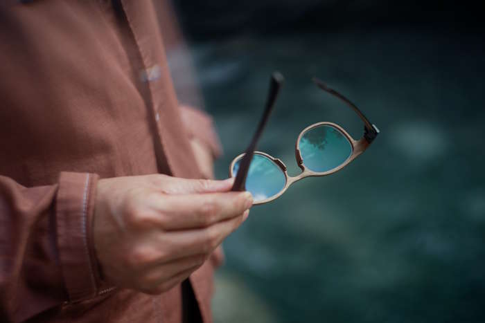 Hand hält eine runde Holzbrille mit blauen Gläsern – Made in Tirol