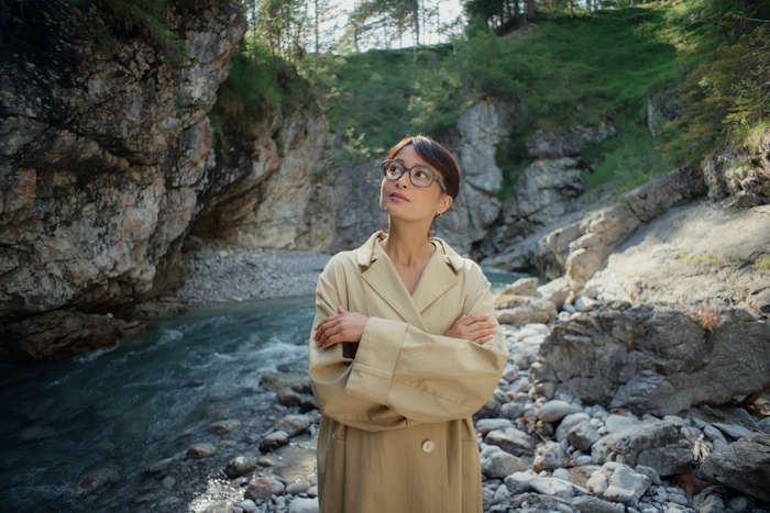 Frau mit Brille an einem Fluss – Hörgeräte und Brillen für klare Sicht auf Reisen