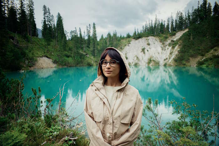 Eine Frau mit nachhaltiger Brille vor einem türkisblauen See.