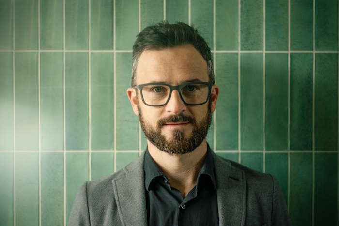 Mann mit dunkler Gleitsichtbrille für Männer vor grün gekachelter Wand