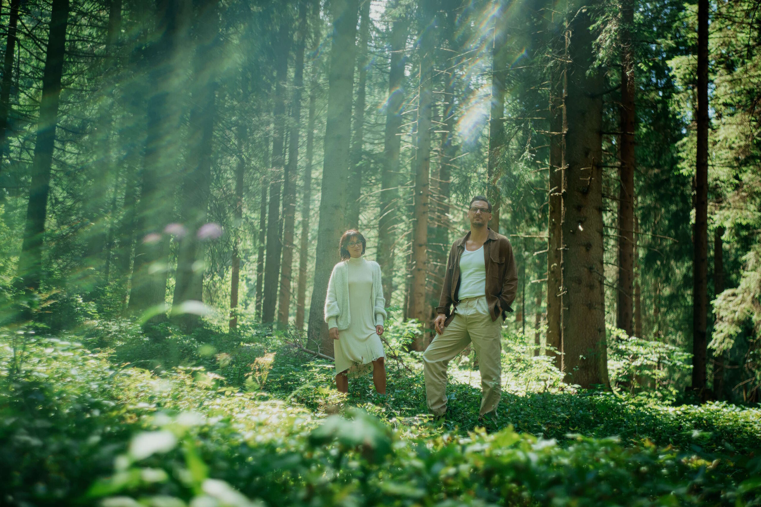 Ein Mann und eine Frau mit Brillen stehen im Sonnenlicht eines dichten Waldes – Symbolbild für die Langlebigkeit von Brillen in natürlicher Umgebung.