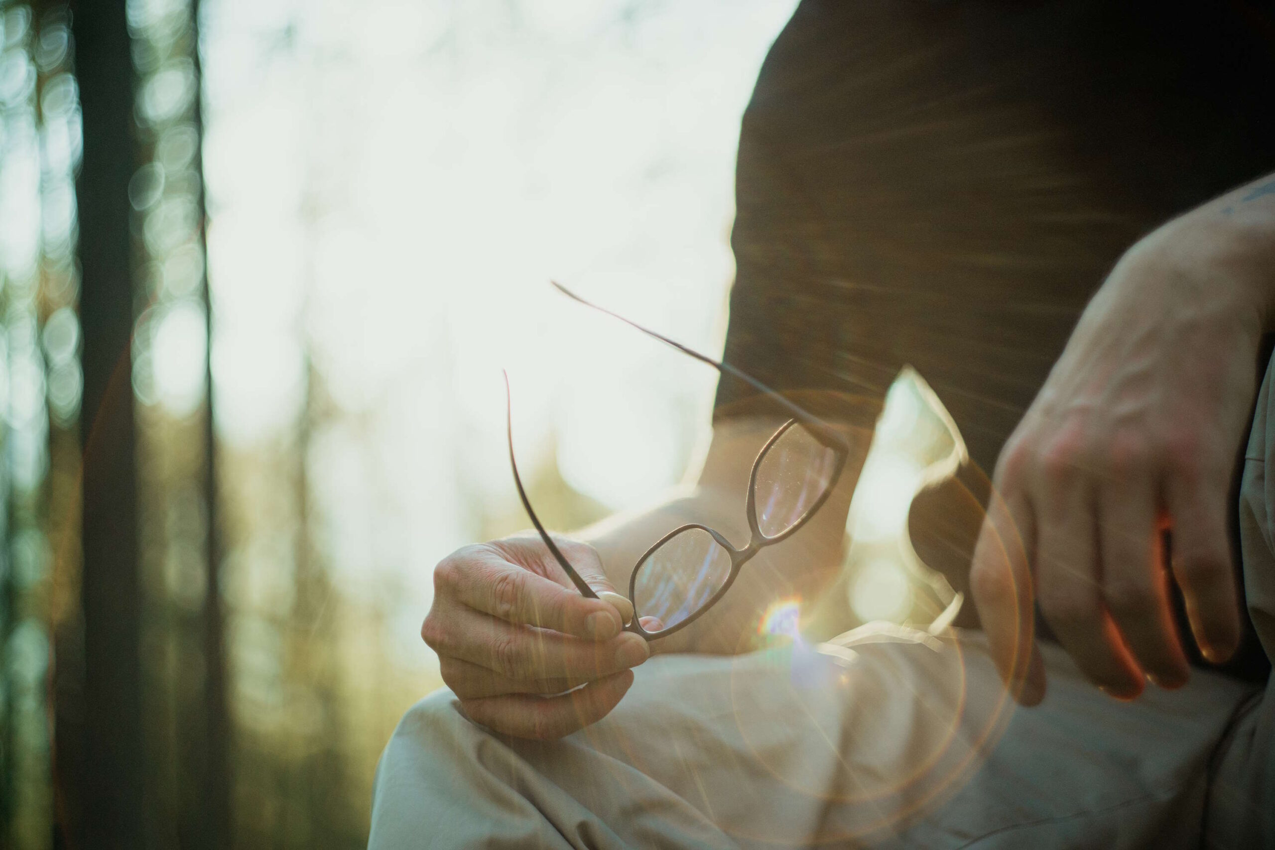 Mann hält eine Gleitsichtbrille für Männer im Sonnenlicht sitzend im Wald