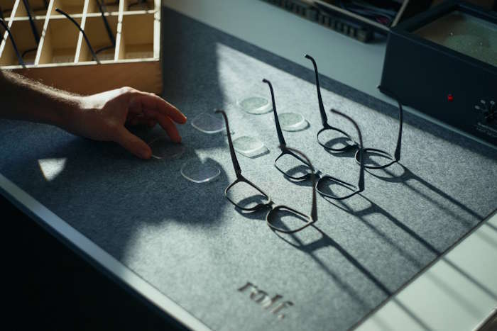 Brillenrahmen und Gläser auf Werkbank mit Hand – Wie entsteht eine Brille?