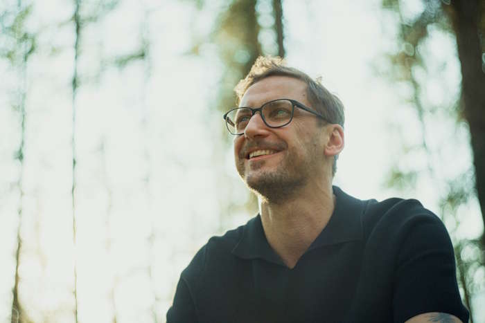 Lachender Brillenträger mit Bart sitzt im Wald in der Sonne