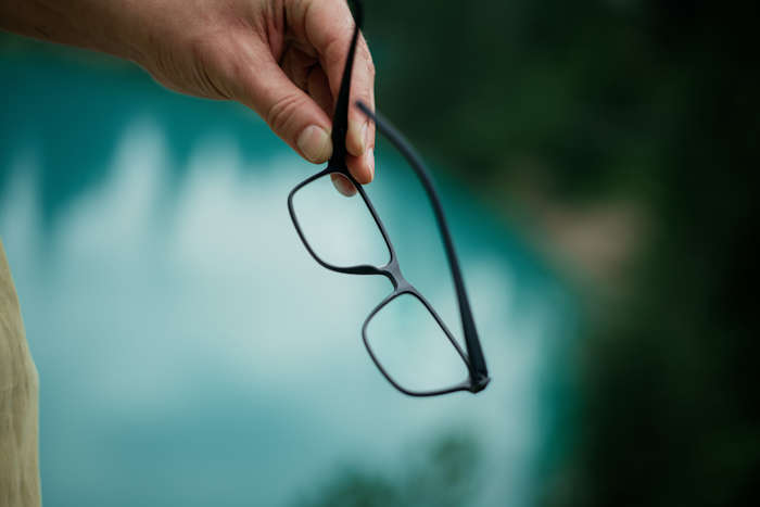 Hand hält eckige schwarze Brille vor See – funktionale Brillen für eckige Gesichter